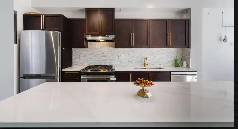 Kitchen renovation by PS Tiling, photo from a Google review: dark cabinets, white quartz counters and a grey mosaic backsplash, finished.