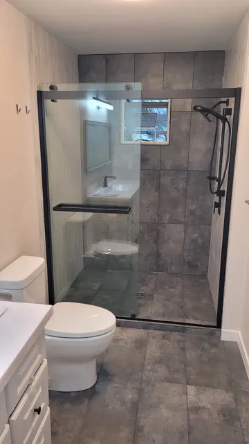 Bathroom renovation by PS Tiling, photo from a Google review: black-framed sliding glass shower with grey porcelain walls and floor, finished.