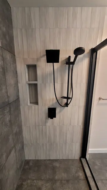 Bathroom renovation by PS Tiling, photo from a Google review: shower wall in white stacked tile with a black rain head, hand shower and recessed niche, finished.