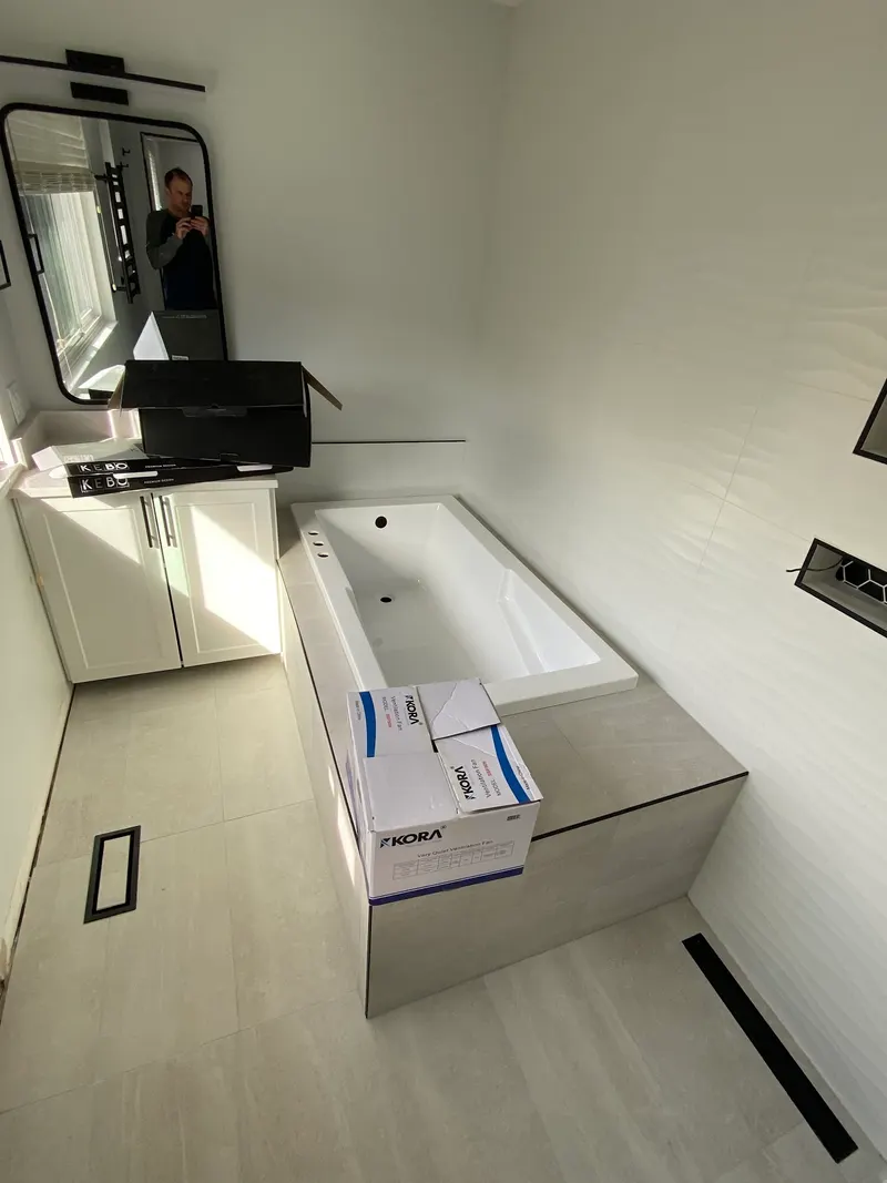 Bathroom renovation by PS Tiling, photo from a Google review: tiled tub deck in grey porcelain, white wave-texture walls and a black-framed mirror, mid-renovation.