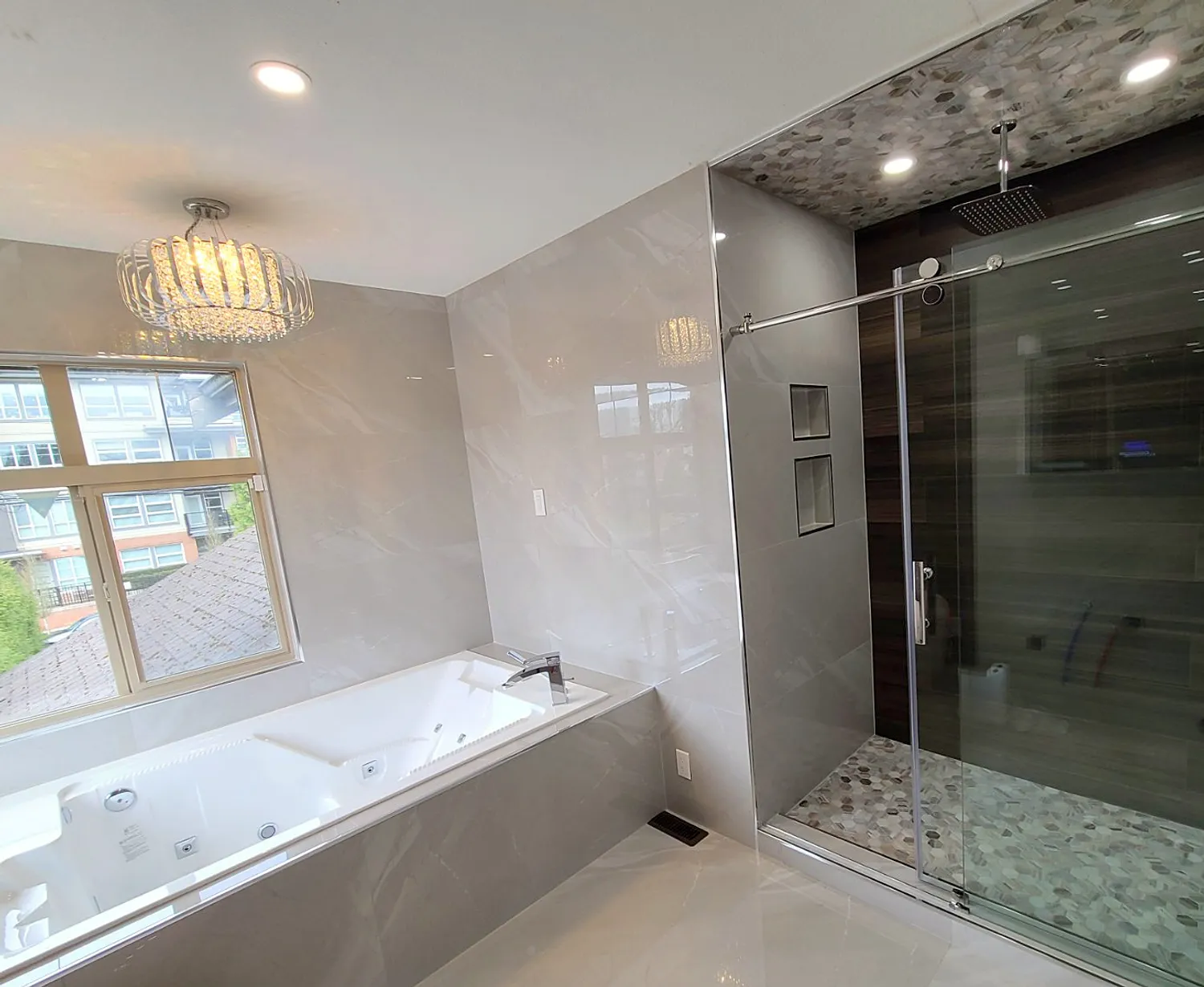 Bathroom renovation in Coquitlam by PS Tiling: crystal chandelier over the jacuzzi tub with the frameless glass shower and pebble-mosaic floor beside it, finished.