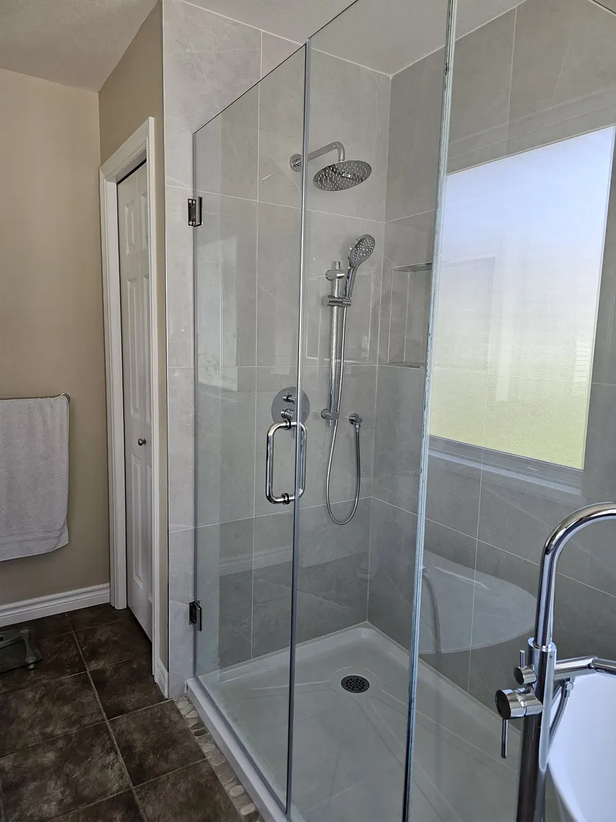 Bathroom renovation in Port Coquitlam by PS Tiling: frameless glass corner shower with grey large-format porcelain walls and a chrome rain shower head, finished.