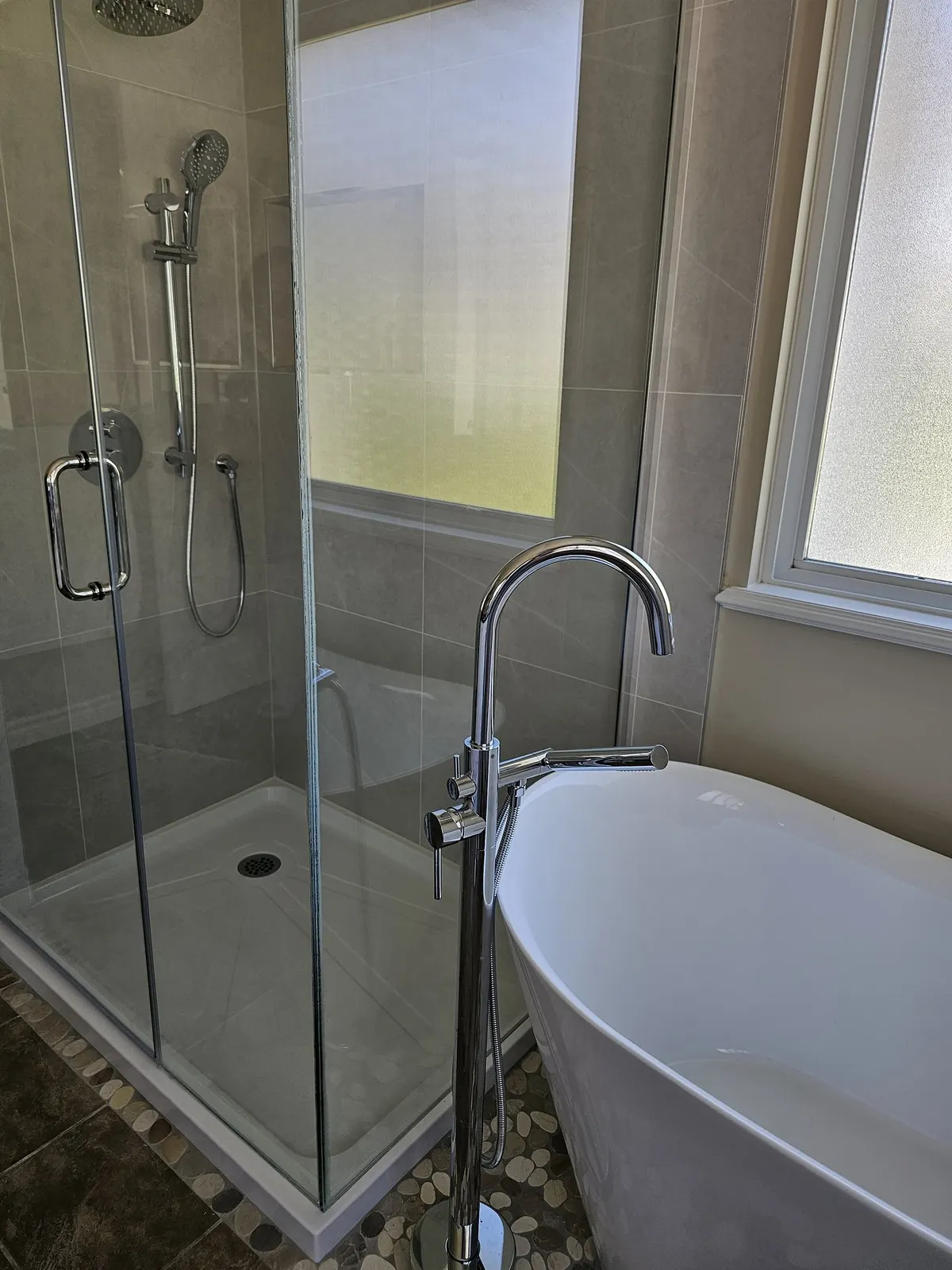 Bathroom renovation in Port Coquitlam by PS Tiling: frameless glass shower beside a freestanding tub with a chrome floor-mount filler, finished.