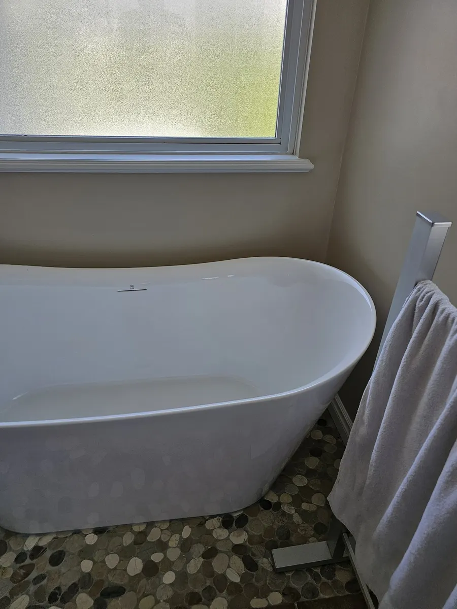 Bathroom renovation in Port Coquitlam by PS Tiling: freestanding soaker tub by the window on a pebble-mosaic floor, finished.