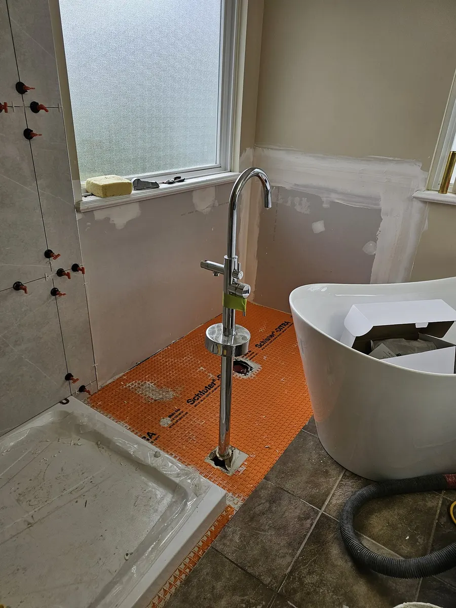Bathroom renovation in Port Coquitlam by PS Tiling: Schluter Kerdi waterproofing membrane on the new shower pan beside the freestanding tub, mid-renovation.