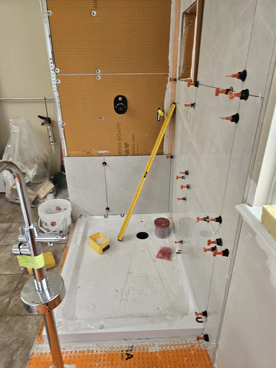 Bathroom renovation in Port Coquitlam by PS Tiling: large-format grey porcelain wall tile going up with levelling clips over the waterproofed shower pan, during tiling.