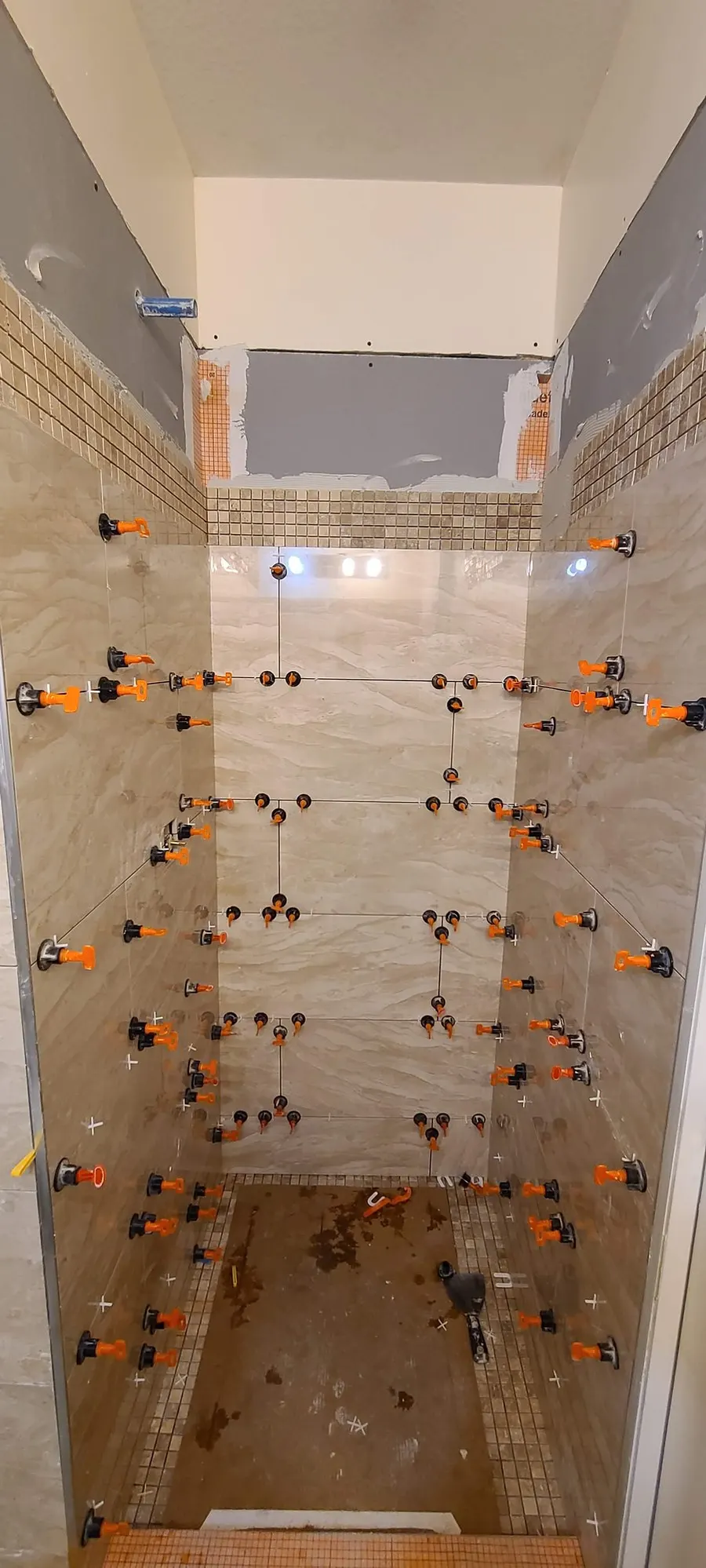 Bathroom renovation in Port Coquitlam by PS Tiling: shower stall wall tile with levelling clips and a mosaic band, during wall tiling.