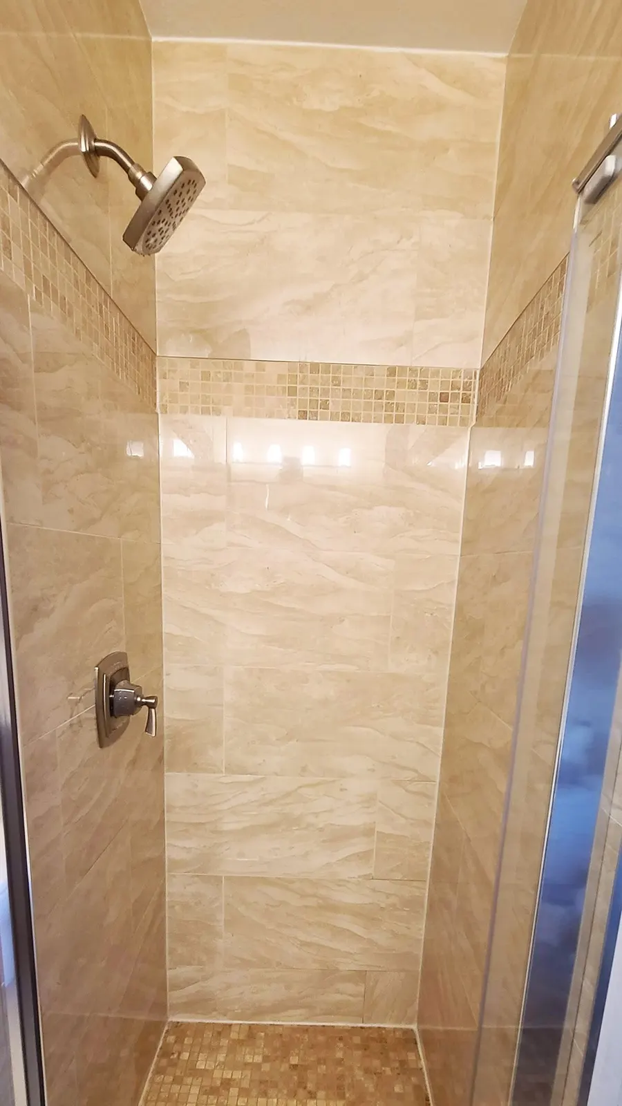 Bathroom renovation in Port Coquitlam by PS Tiling: tub surround in beige marble-look porcelain with a mosaic accent band and chrome shower head, finished.