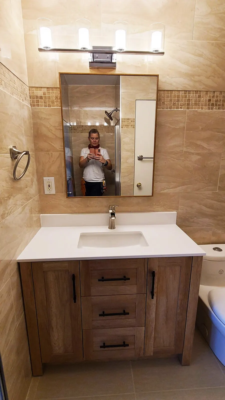 Bathroom renovation in Port Coquitlam by PS Tiling: wood vanity with a white top and framed mirror between tiled walls, finished.