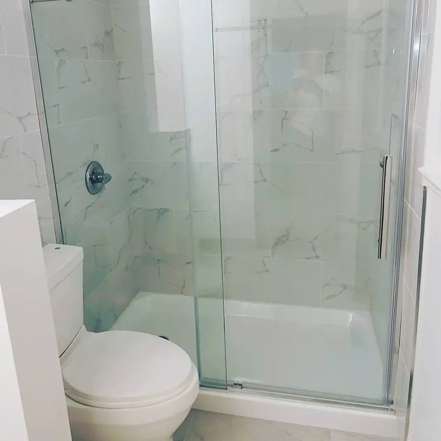 Condo bathroom renovation in Fairview, Vancouver by PS Tiling: marble-look shower with sliding glass door and toilet, finished.
