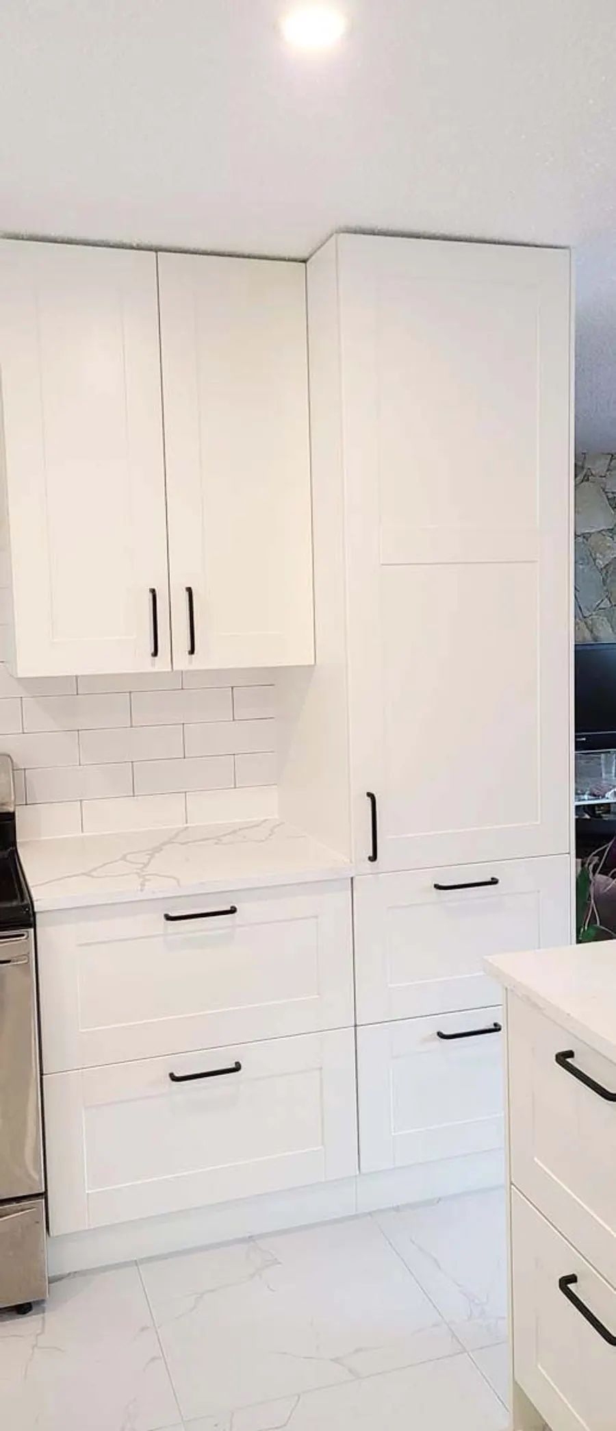 Kitchen renovation in Port Moody by PS Tiling: tall white pantry cabinets with black handles beside the island, finished.