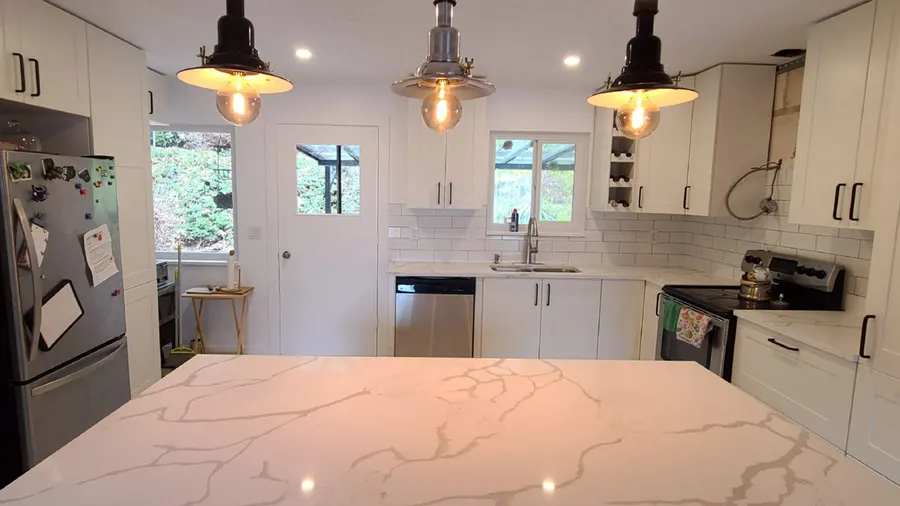 Kitchen renovation in Port Moody by PS Tiling: white quartz island and pendant lights with the sink wall behind, finished.