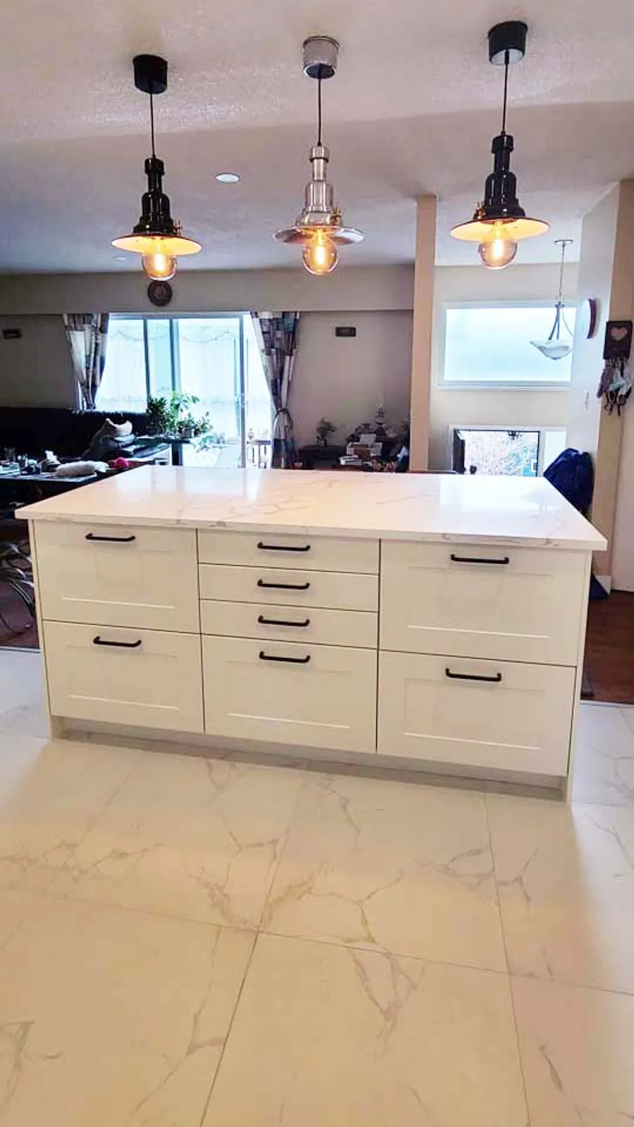 Kitchen renovation in Port Moody by PS Tiling: white quartz island with three pendant lights and marble-look porcelain floor, finished.