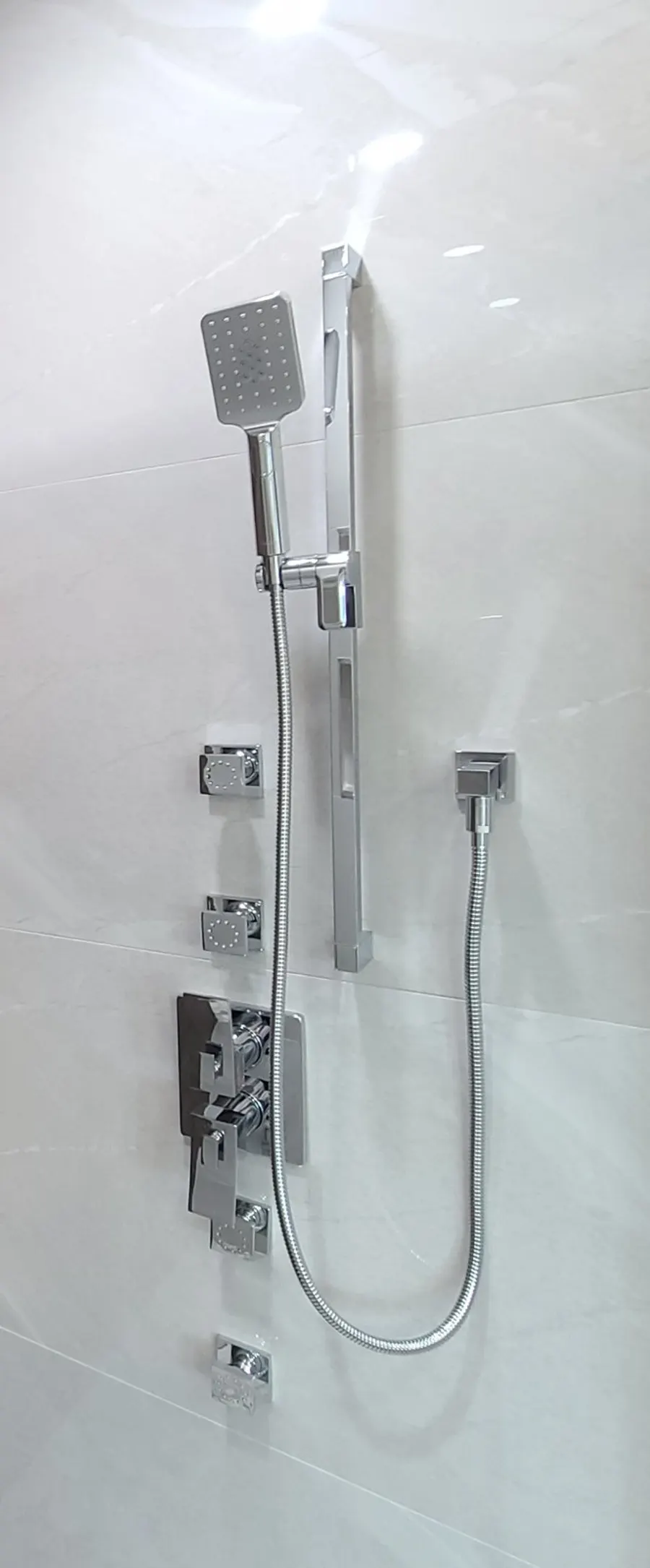 Master bathroom renovation in Burquitlam, Coquitlam by PS Tiling: chrome body-jet shower panel with rain head and hand shower on marble-look tile, detail.