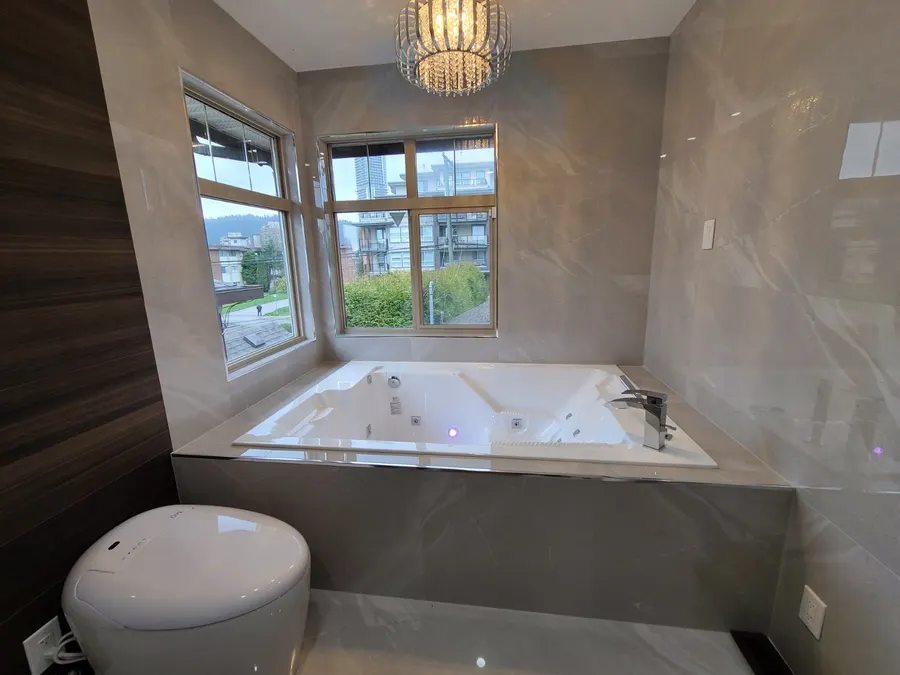 Master bathroom renovation in Burquitlam, Coquitlam by PS Tiling: corner jacuzzi tub framed by windows under a crystal chandelier, finished.
