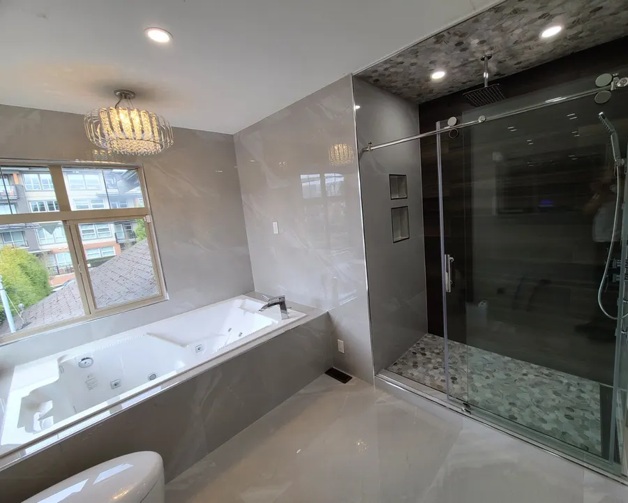 Master bathroom renovation in Burquitlam, Coquitlam by PS Tiling: crystal chandelier over the jacuzzi tub with the frameless sliding glass shower beside it, finished.