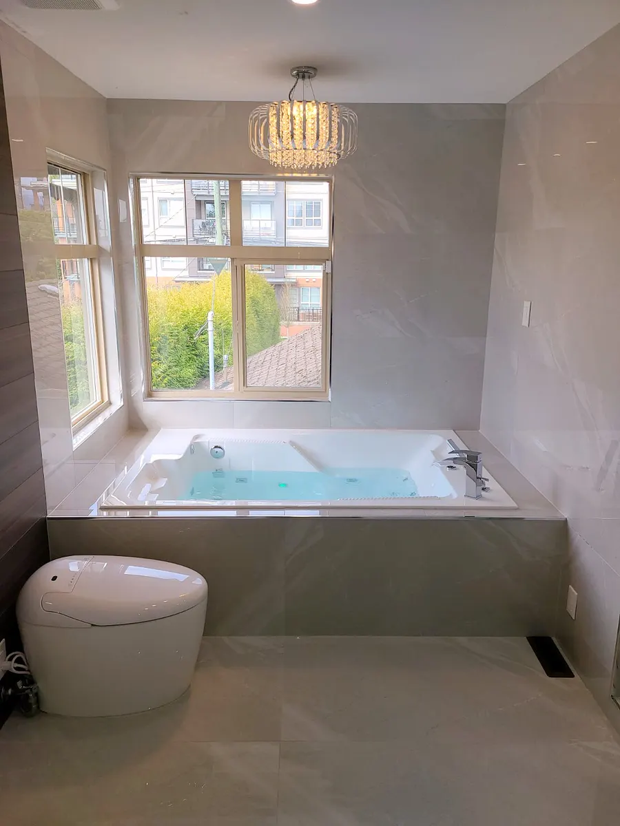 Master bathroom renovation in Burquitlam, Coquitlam by PS Tiling: jacuzzi tub set in large-format marble-look porcelain with the smart toilet in front, finished.