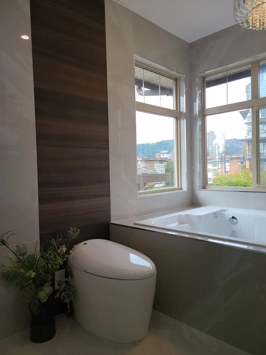 Master bathroom renovation in Burquitlam, Coquitlam by PS Tiling: ÖVE smart toilet against a dark wood-look porcelain accent wall by the window, finished.