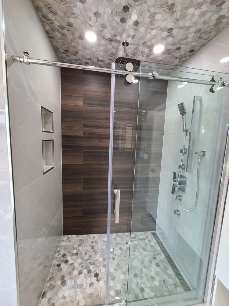 Bathroom renovation in Coquitlam by PS Tiling, sliding glass shower with a pebble floor sloping to the drain and a wood-look wall, finished.