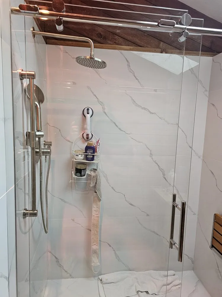 Shower renovation in Fort Langley by PS Tiling, a frameless glass swing door with a chrome handle on marble-look tile, finished.