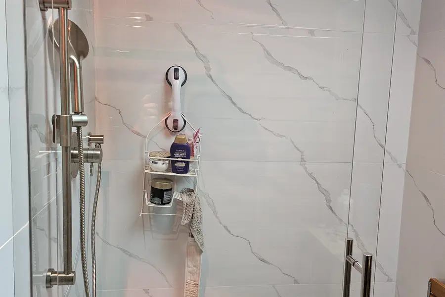 Shower renovation in Fort Langley by PS Tiling: frameless glass shower door with chrome handle and marble-look porcelain walls, finished.