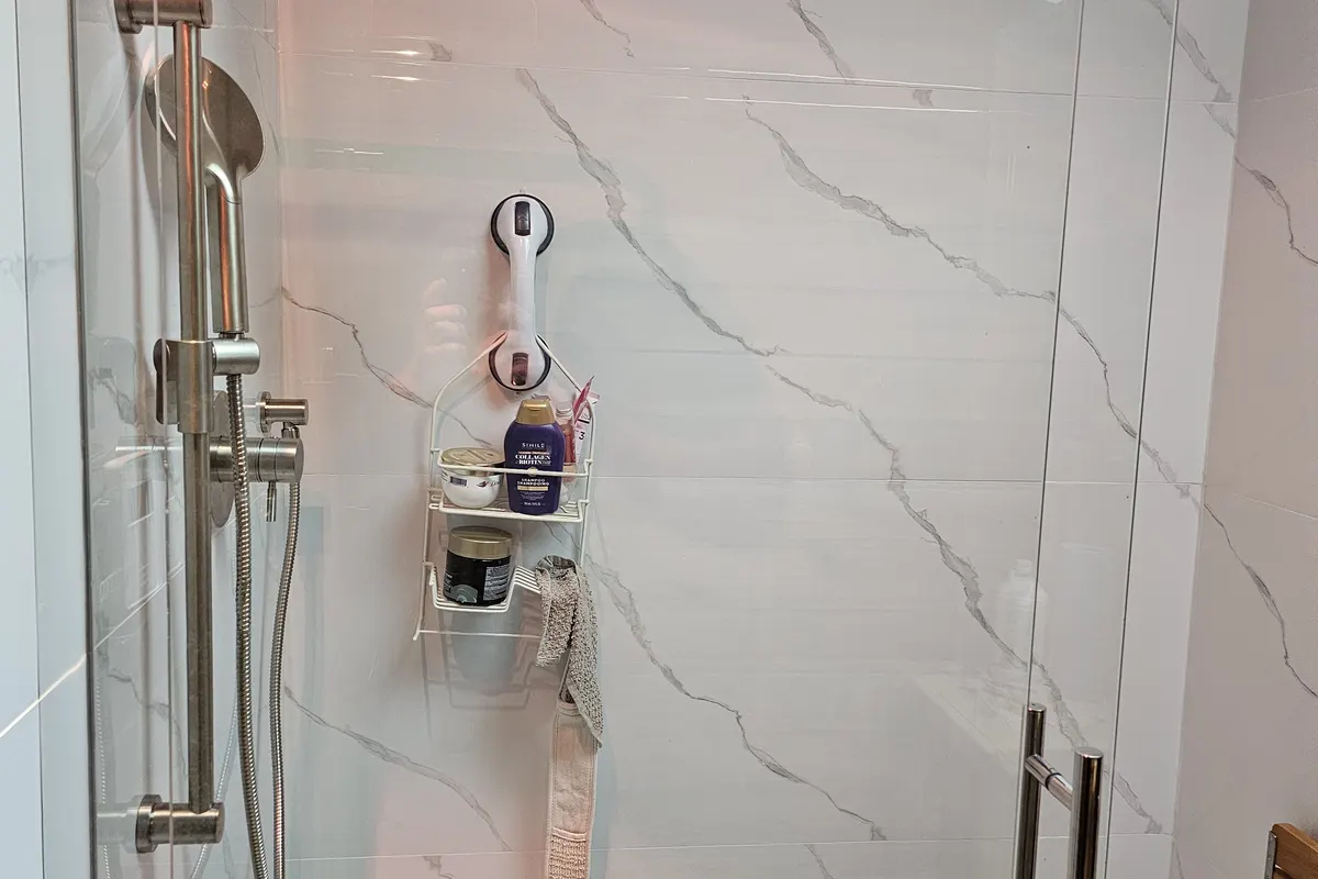 Shower renovation in Fort Langley by PS Tiling: frameless glass shower door with chrome handle and marble-look porcelain walls, finished.