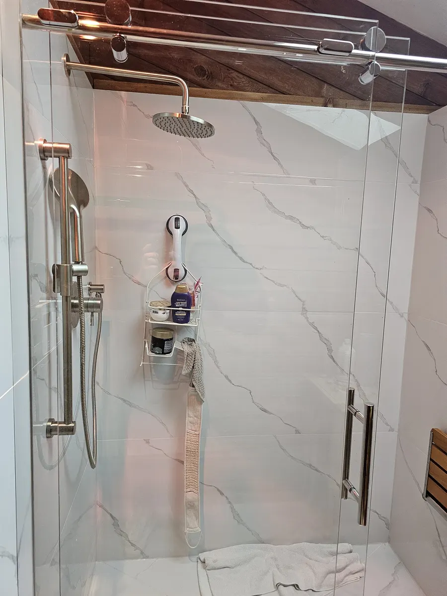 Shower renovation in Fort Langley by PS Tiling: frameless glass shower door with chrome handle and marble-look tile, finished.