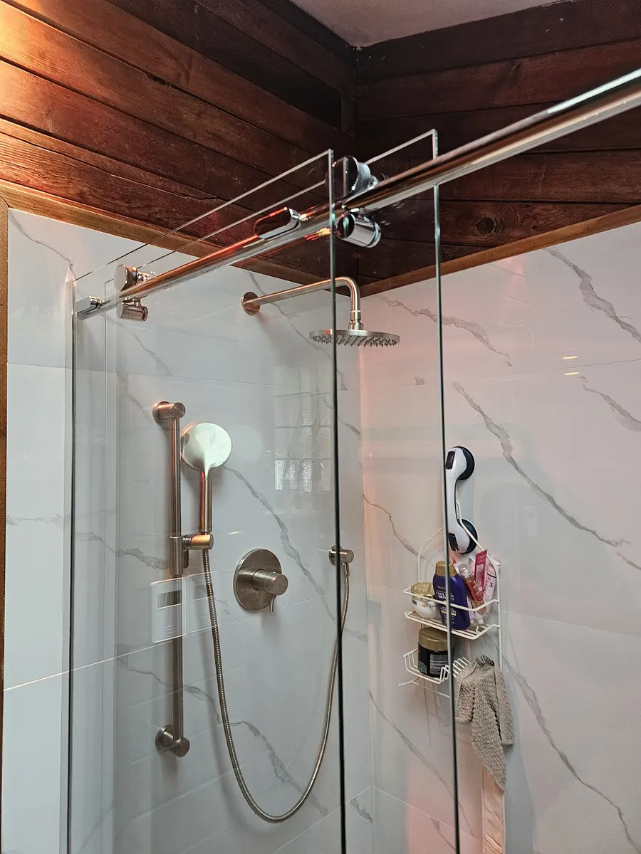 Shower renovation in Fort Langley by PS Tiling: frameless glass shower with marble-look porcelain walls, chrome rain head and a wood plank ceiling, finished.