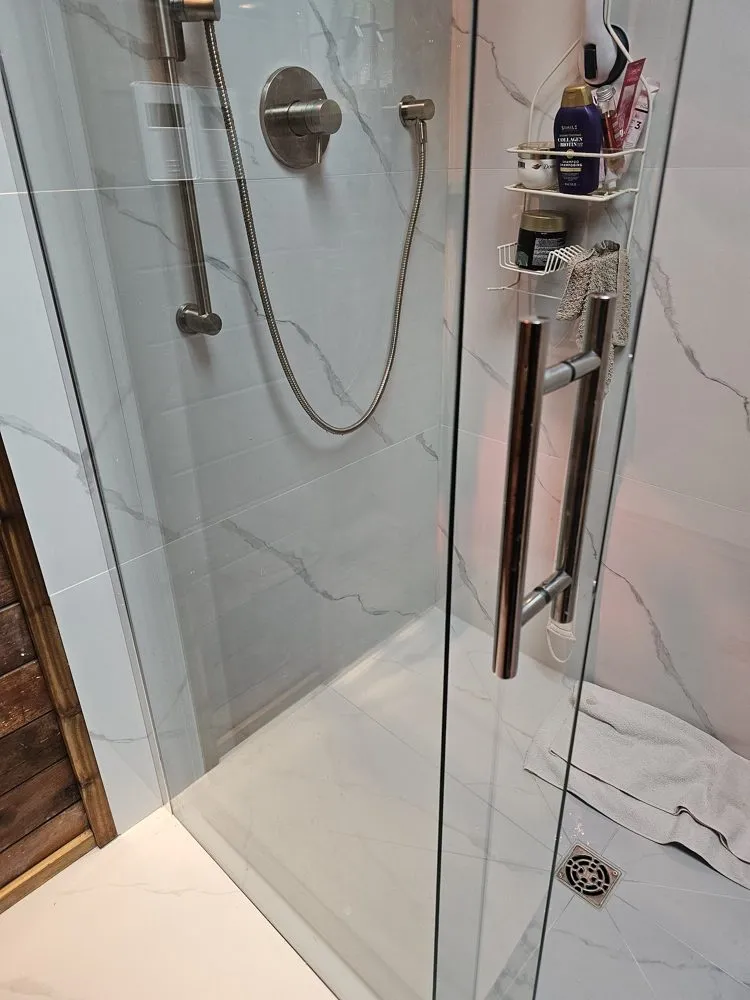 Shower renovation in Fort Langley by PS Tiling, a chrome rain head and hand shower on marble-look tile, finished.