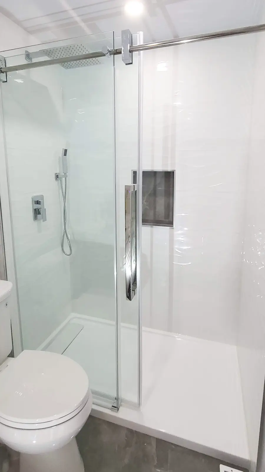 Tub-to-shower conversion in Coquitlam by PS Tiling: frameless sliding glass shower with a rain head and a grey marble-look niche, finished.