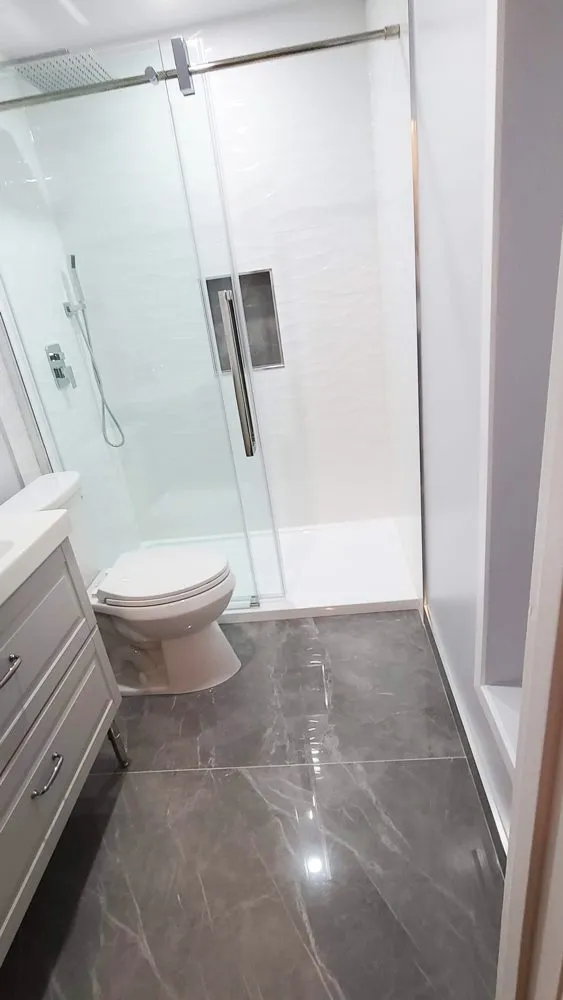Tub-to-shower conversion in Coquitlam by PS Tiling, a walk-in shower with white wave tile and a grey floor where the tub used to be, finished.