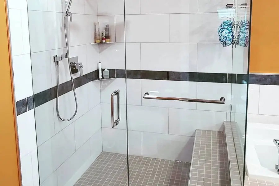 Shower renovation in Delta by PS Tiling: frameless glass shower with tiled bench, white tile and a black accent band, finished.