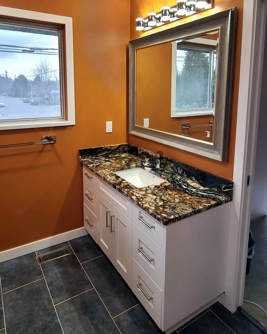Shower renovation in Delta by PS Tiling: white vanity with a dark stone top and framed mirror on an orange wall, finished.