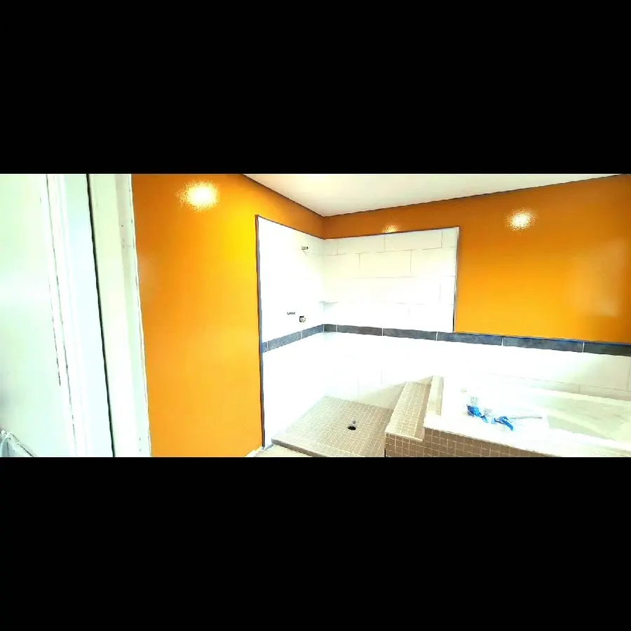 Shower renovation in Delta by PS Tiling: white wall tile with a black accent band against orange walls, during wall tiling.